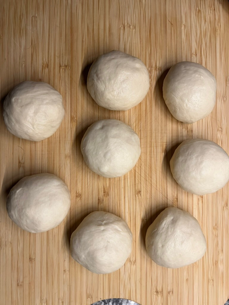 Eight portioned dough balls resting on a wooden board