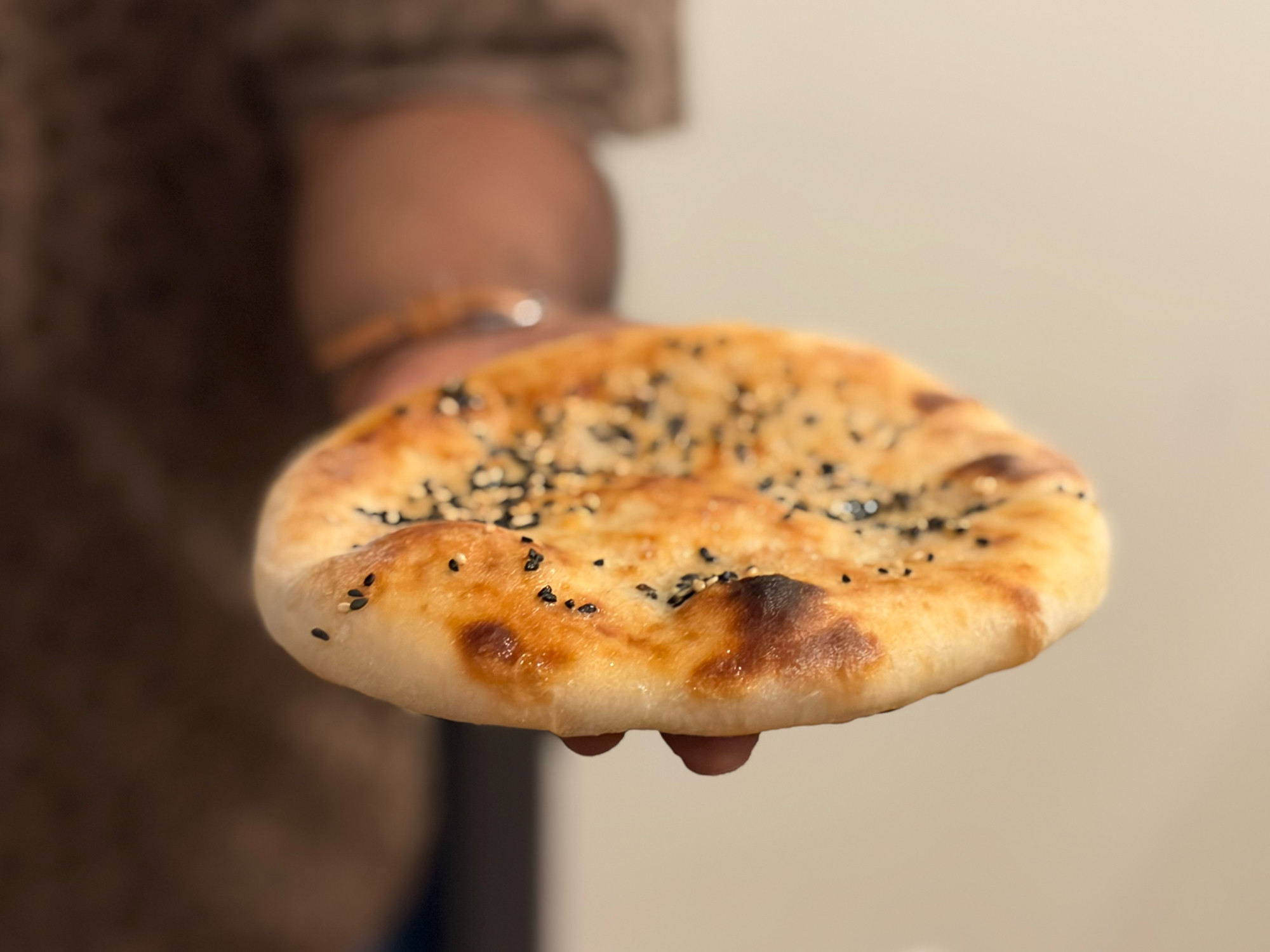 Finished sourdough discard naan, char-spotted and sesame-topped